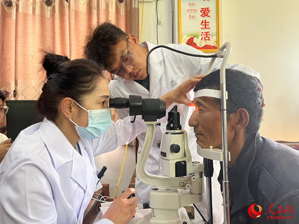 王紅英（左）和團(tuán)隊成員為達(dá)熱村村民檢查眼睛。人民網(wǎng)記者 杜燕飛攝
